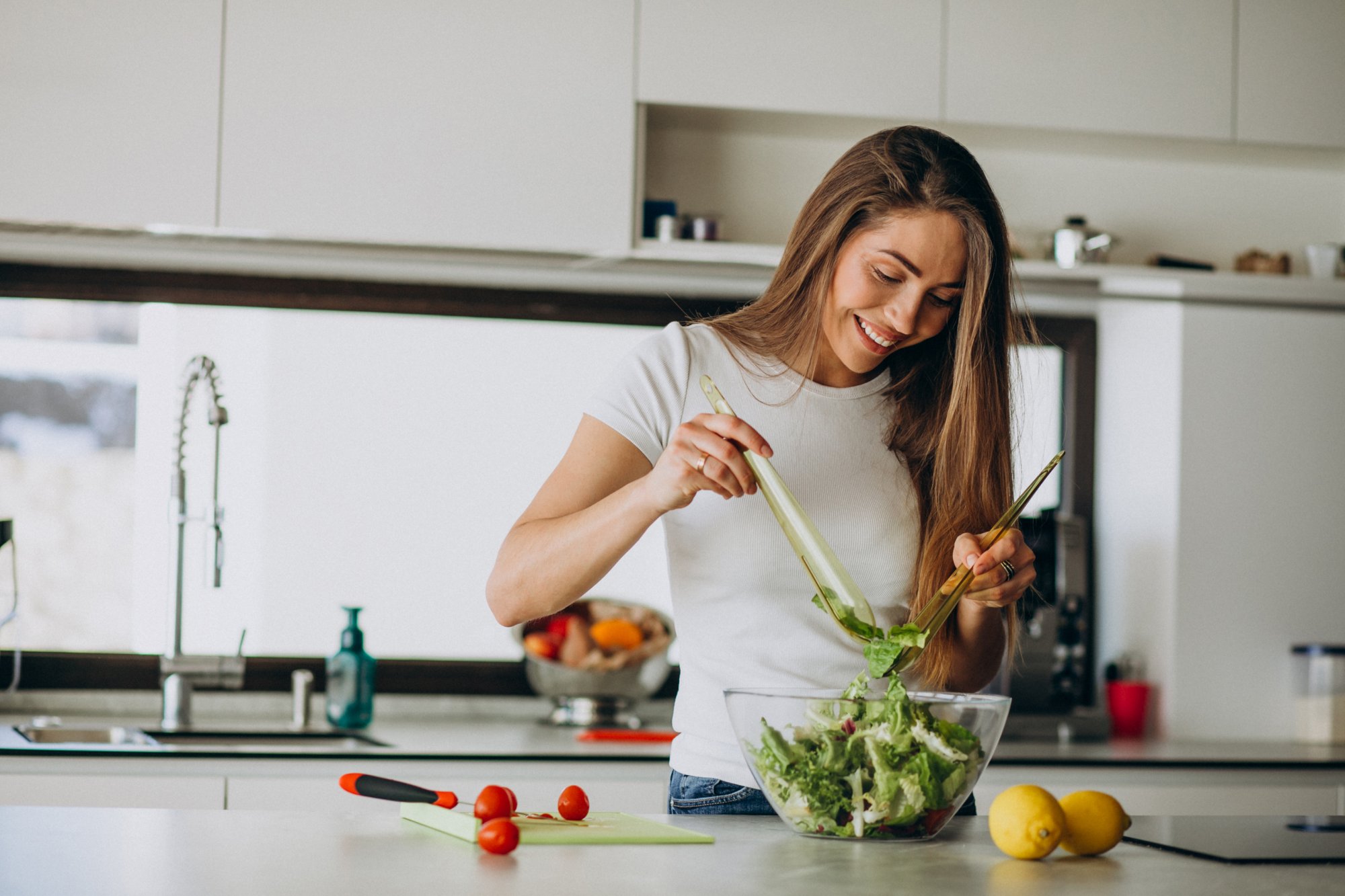 ernaehrung.jpg Frau mischt Salat in einer Schüssel in einer modernen Küche, umgeben von frischen Zutaten.