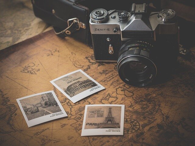 reiseapotheke.jpg Eine analoge Kamera vom Typ Zenit-E steht auf einer alten Weltkarte, umgeben von Polaroid-Fotos von Paris.