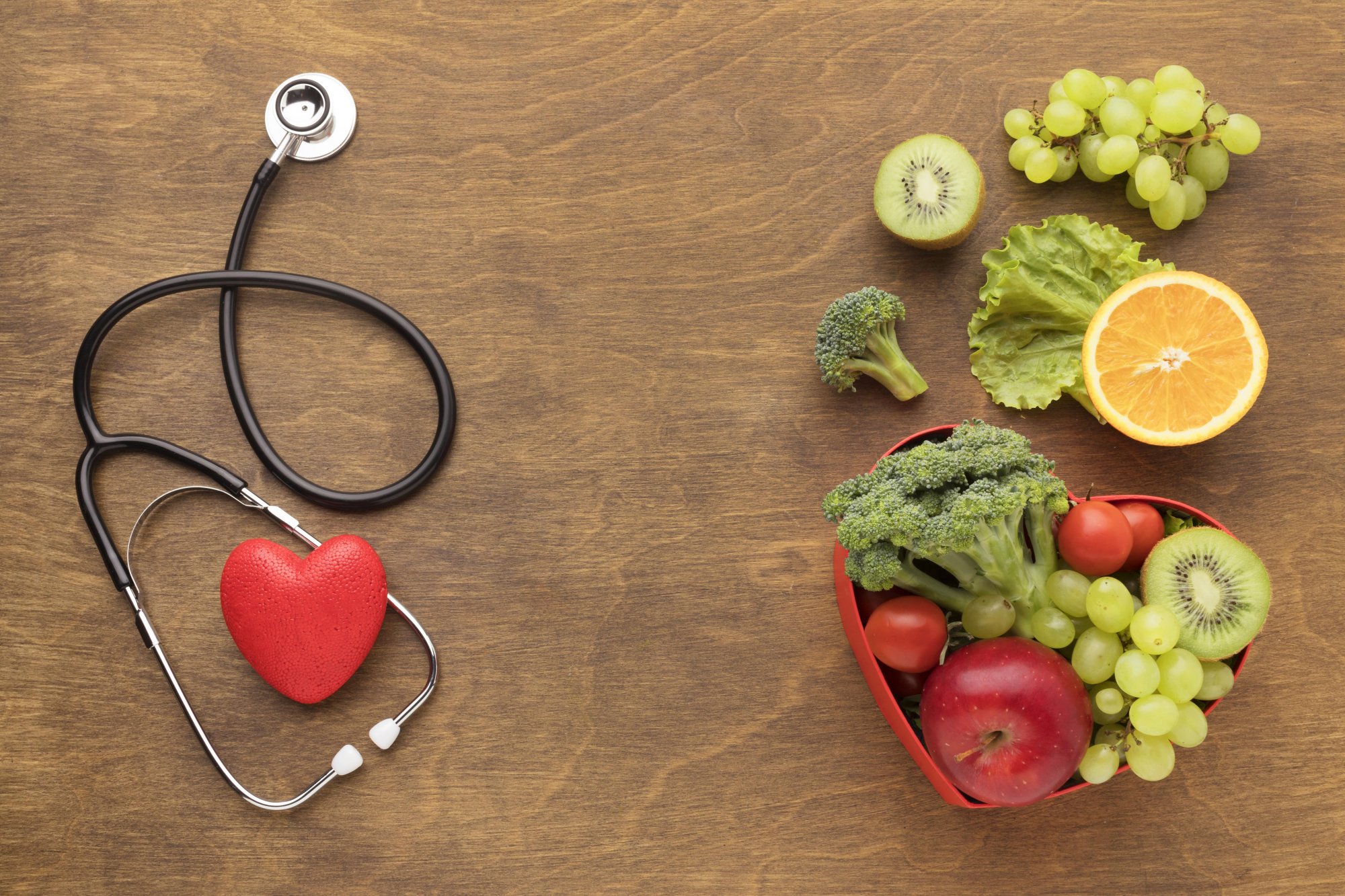 starkes-herz.jpg Ein Stethoskop und ein rotes Herzmodell neben einer herzförmigen Schale mit frischen Obst- und Gemüsesorten.