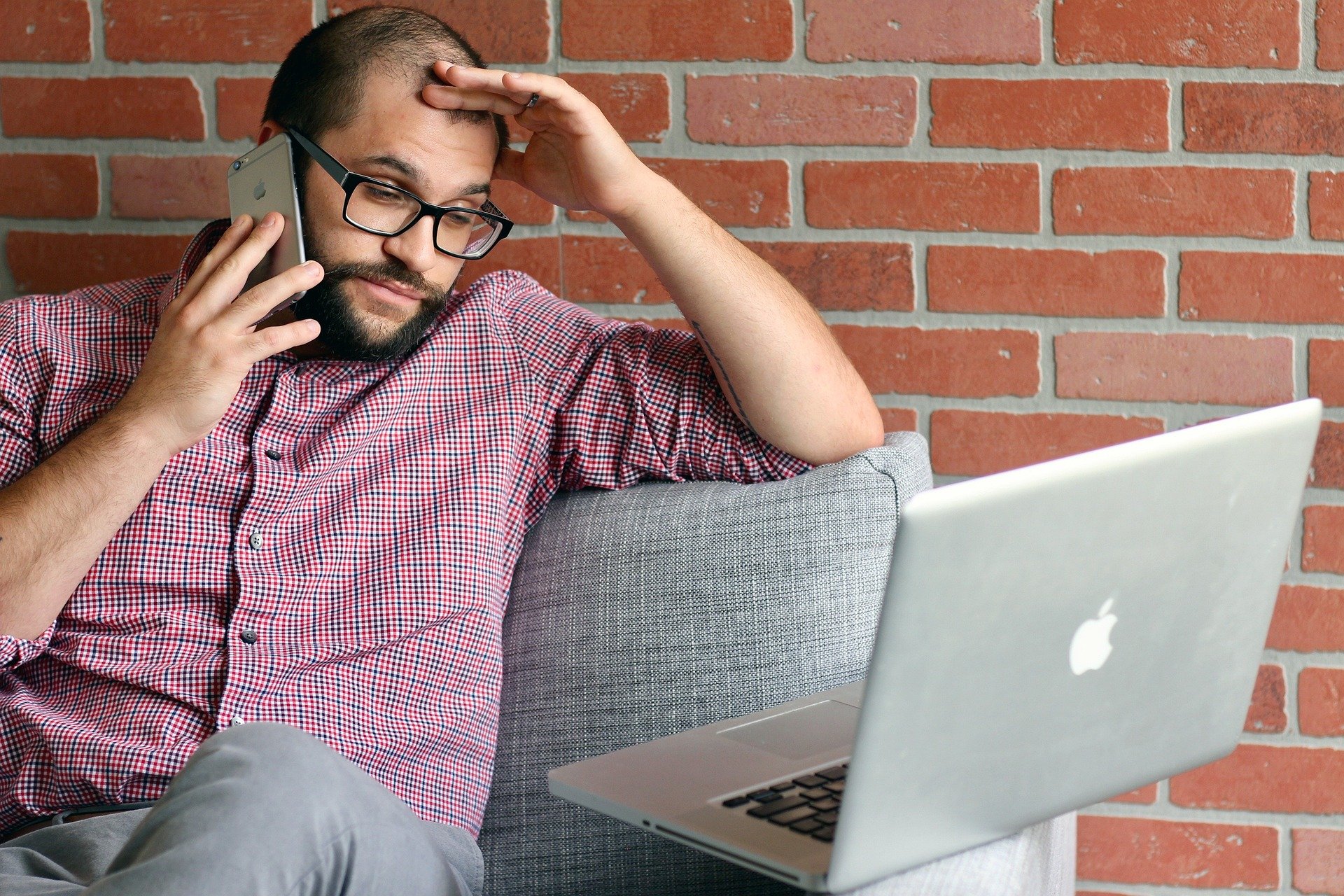 stress-reduktion.jpg Mann mit Brille sitzt auf einem Sofa, telefoniert und schaut besorgt auf einen Laptop.