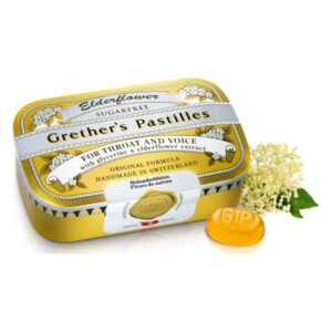 Runde, gelbe Bonbons in einer goldenen Blechdose mit einer Abbildung von Holunderblüten.