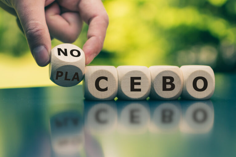 Holzwürfel mit Buchstaben, die das Wort 'NO PLACEBO' bilden, auf einem Tisch in der Natur.